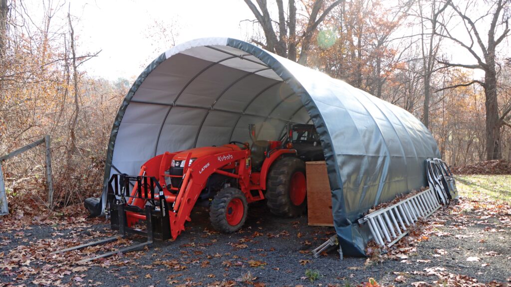orange tractor being stored under portable garage shelter